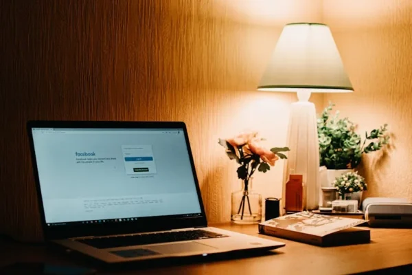 Warmly lit workspace featuring a laptop open to Facebook, a lamp, and decorative items.