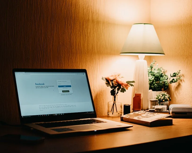 Warmly lit workspace featuring a laptop open to Facebook, a lamp, and decorative items.
