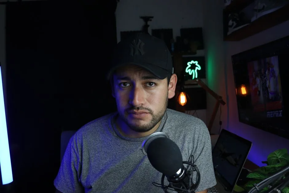 Male content creator in a home studio setup with microphone and soft lighting.