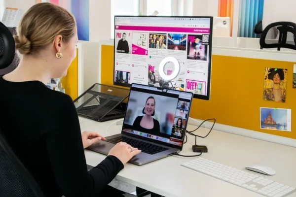 A woman conducts a professional video call while working at her desk in a bright office setting.